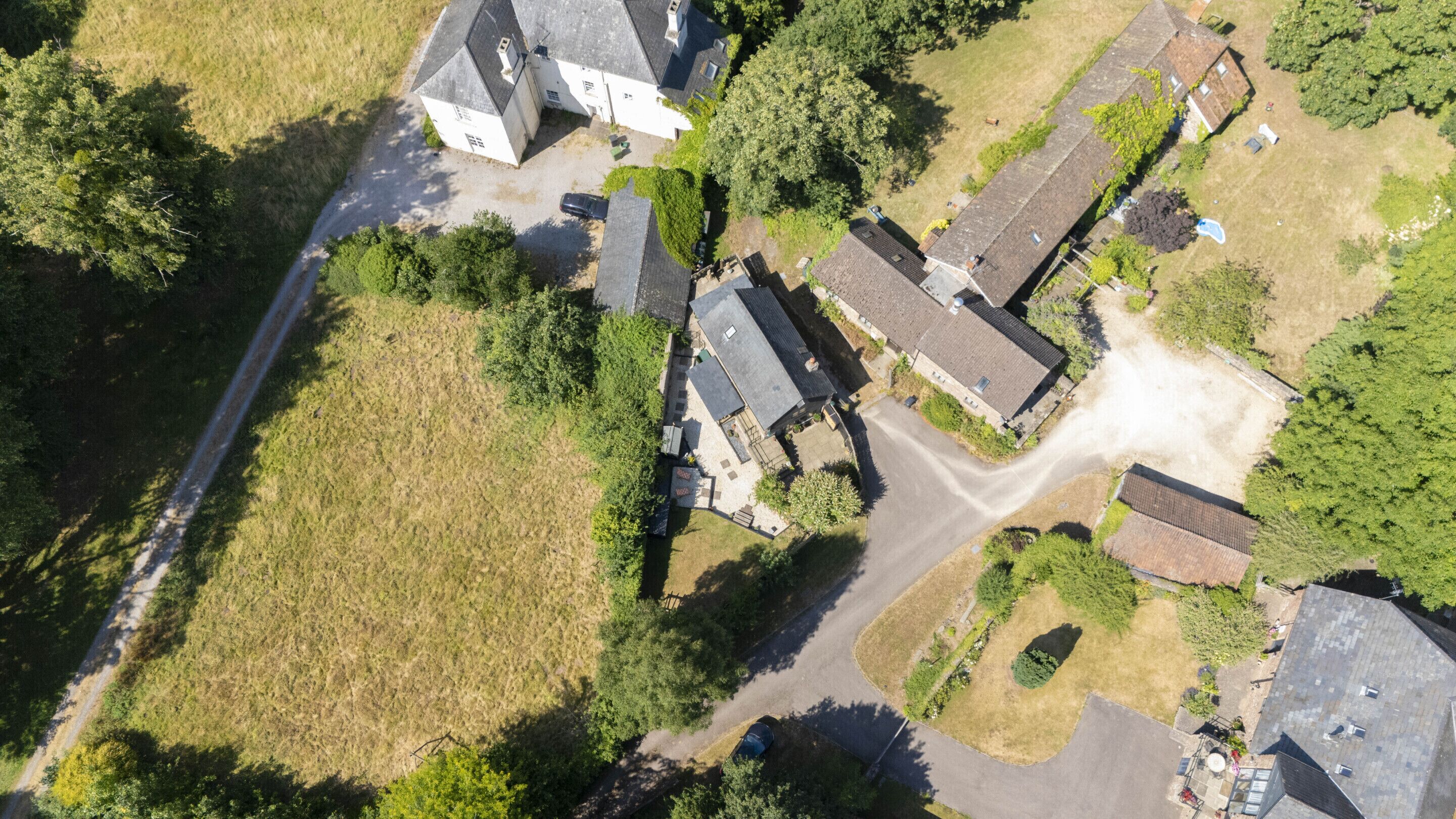 An aerial view of a residential area with houses, a road, and surrounding greenery.