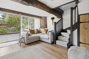 A cozy living room with a sectional sofa, a staircase, and a view of the garden. - The Tractor Shed: A Quiet Retreat Near Symonds Yat (Ross-on-Wye)