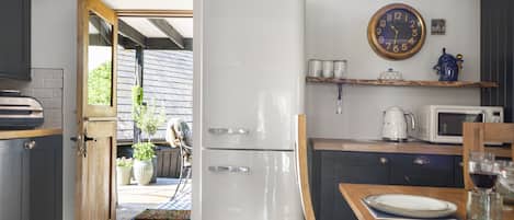 Een keuken met een witte koelkast, een houten eettafel met een bord en een glas, en een klok aan de muur.
