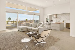 Ein modernes Interieur mit einem großen, winkelförmigen Sofa, einem Essbereich und einer Küche mit Blick ins Freie.