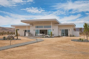 Ein modernes, zweistöckiges Haus mit flachem Dach, großen Fenstern und einer Terrassenfläche.