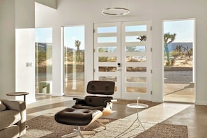 A modern living room with a leather sofa, a coffee table, and a large window with a view of a desert landscape. - Sage Space By Homestead Modern (Yucca Valley)