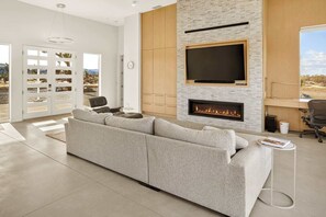 Ein modernes Wohnzimmer mit einem großen Ecksofa, einem Kamin, einem Flachbildfernseher und Blick auf die Wüstenlandschaft durch Glasschiebetüren.
