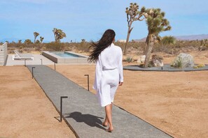 A person walking on a concrete path in a desert landscape with cacti and a pool. - Sage Space By Homestead Modern (Yucca Valley)