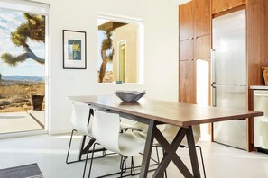 A modern kitchen with a wooden table, white chairs, and a view of a desert landscape. - Shelter 1 by Homestead Modern (Joshua Tree)