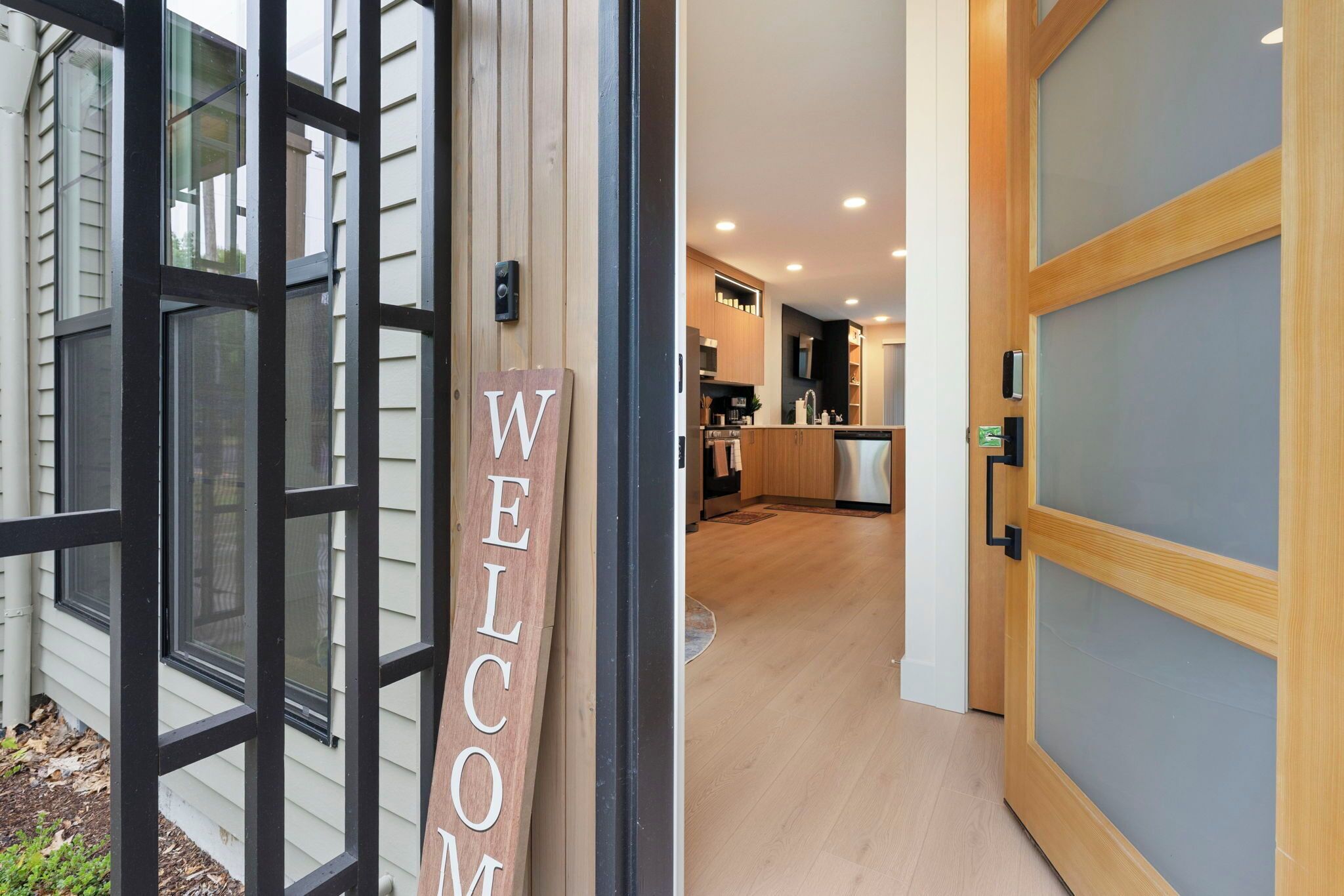 Fachada moderna com um letreiro 'WELCOME', uma porta de madeira com painel de vidro jateado e uma cozinha com armários de madeira e eletrodomésticos de aço inoxidável.