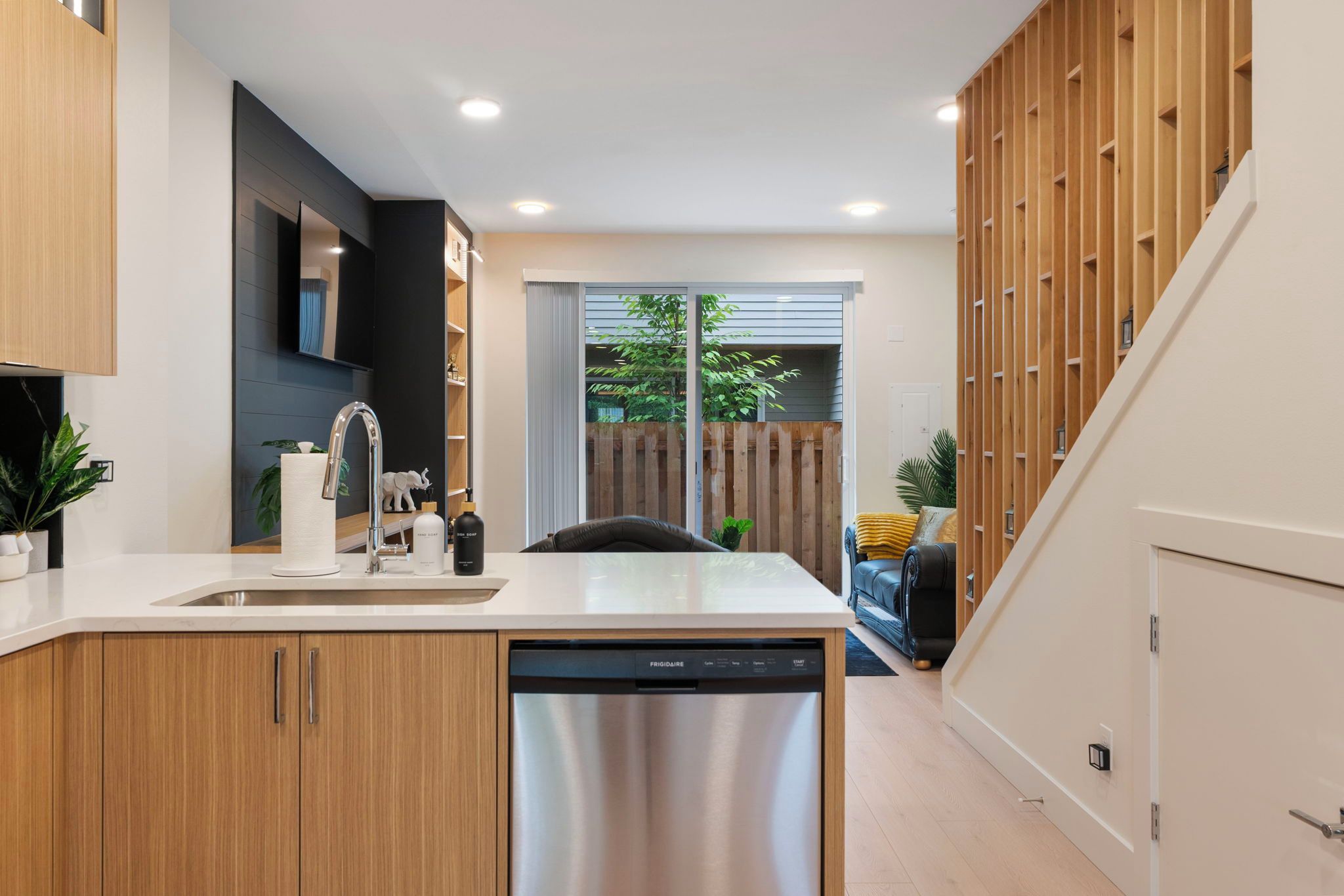 A modern kitchen with a dishwasher, a sink, and a countertop. There is a wooden cabinet and a plant on the counter.