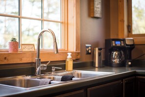 A kitchen with a stainless steel sink, a coffee maker, and a window with a view of trees. - Charming 3-bedroom, 3 bathroom house in a peaceful, cozy place with AC. (Parkers Prairie)