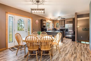 A modern kitchen with a central island, stainless steel appliances, and a dining area with wooden chairs and a table. - Charming 3-bedroom, 3 bathroom house in a peaceful, cozy place with AC. (Parkers Prairie)