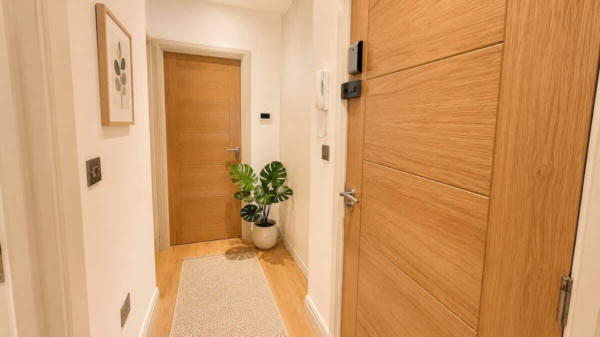 A hallway with wooden doors, a potted plant, and a light switch on the wall.
