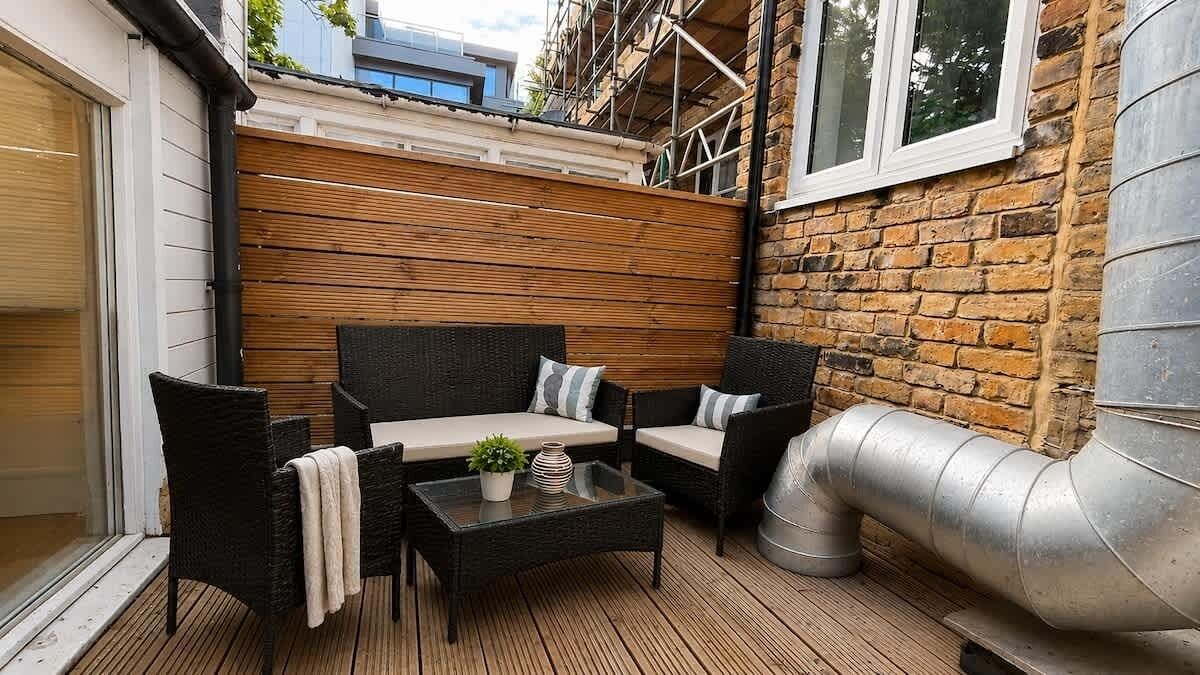 An outdoor patio with wicker furniture, a glass table, and a metal chimney.