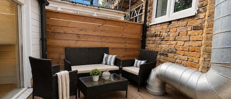 An outdoor patio with wicker furniture, a glass table, and a metal chimney.