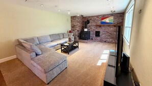 A living room with a sectional sofa, a fireplace, a flat-screen TV, and a carpeted floor. - Woodside Retreat Estate - Home + Guest Barn (Bend)