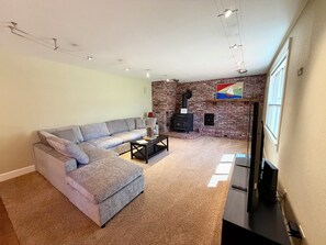 A living room with a sectional sofa, a fireplace, a flat-screen TV, and a carpeted floor. - Woodside Retreat Estate - Home + Guest Barn (Bend)