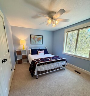 A bedroom with a bed, a ceiling fan, a window, and a wall-mounted lamp. - Woodside Retreat Estate - Home + Guest Barn (Bend)