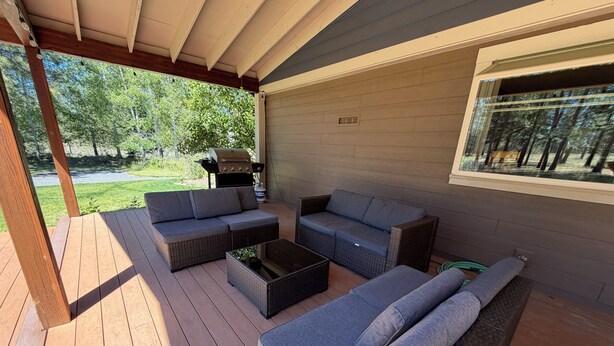 An outdoor patio with wicker furniture, a grill, and a view of a green landscape. - Woodside Retreat Estate - Home + Guest Barn (Bend)