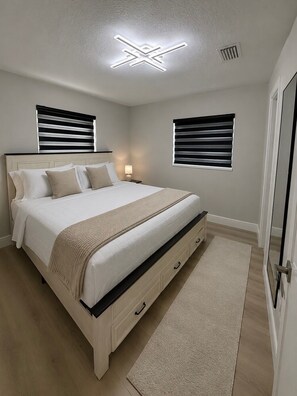 A bedroom with a bed, bedside tables, a ceiling light fixture, and two windows with blinds. - 3-bedroom 2 bath house in serene Tampa 4 min drive from airport (Tampa)
