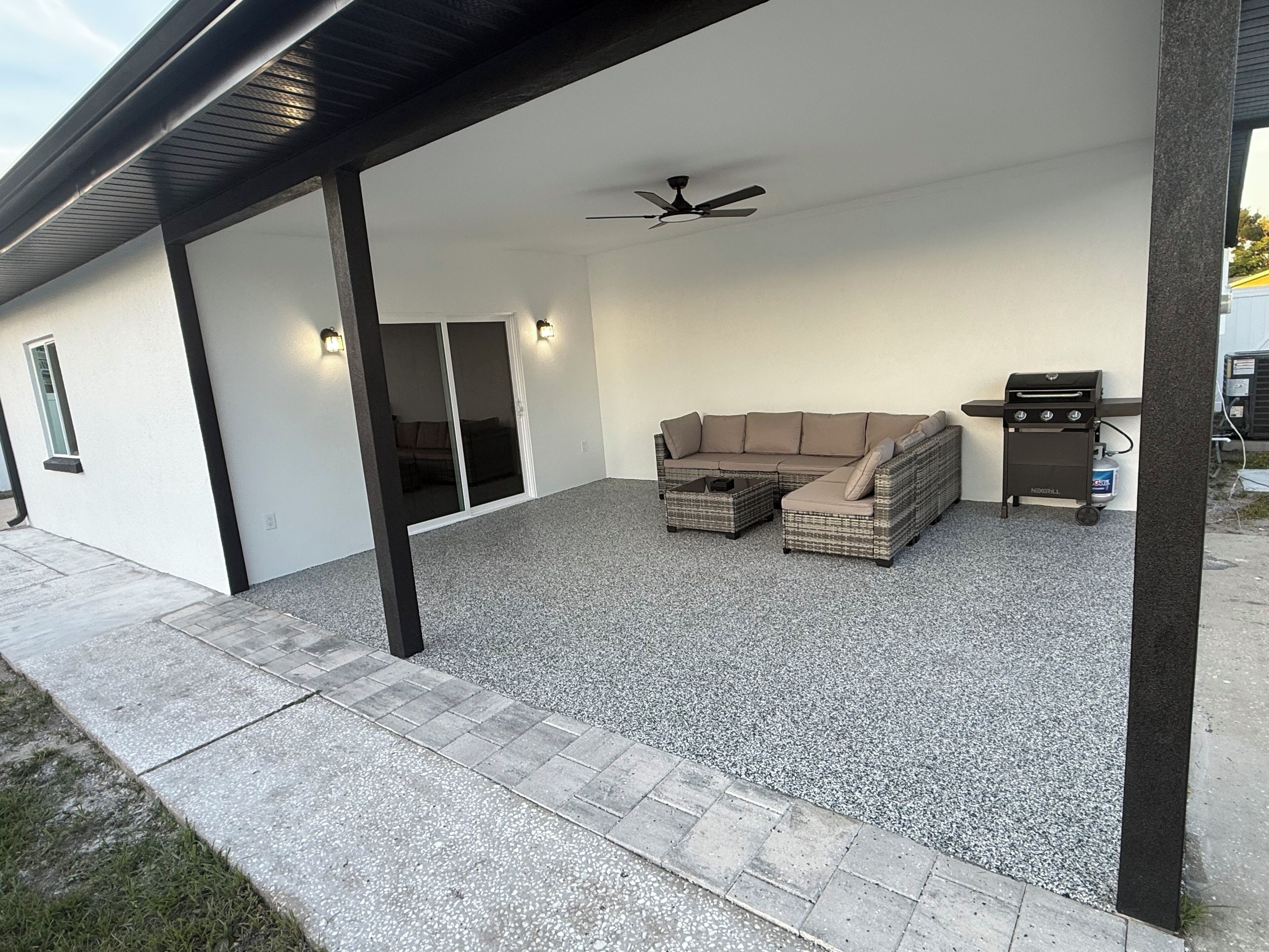 An outdoor patio with a sectional sofa, a ceiling fan, and a grill.