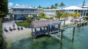 Ein Resort mit Pool, Liegestühlen, einem strohgedeckten Gebäude und einer anlegenden Mole.