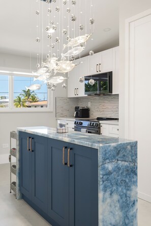 A modern kitchen with a marble island, stainless steel appliances, and a unique chandelier. - Islamorada Waterfront Retreat Private Beach, Boat Lift & Canal Access (Islamorada)