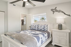 A bedroom with a bed, a nightstand, a lamp, a ceiling fan, and a wall decoration. - Islamorada Waterfront Retreat Private Beach, Boat Lift & Canal Access (Islamorada)