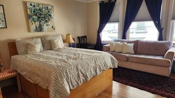 A bedroom with a bed, a sofa, a painting, and a window with curtains.