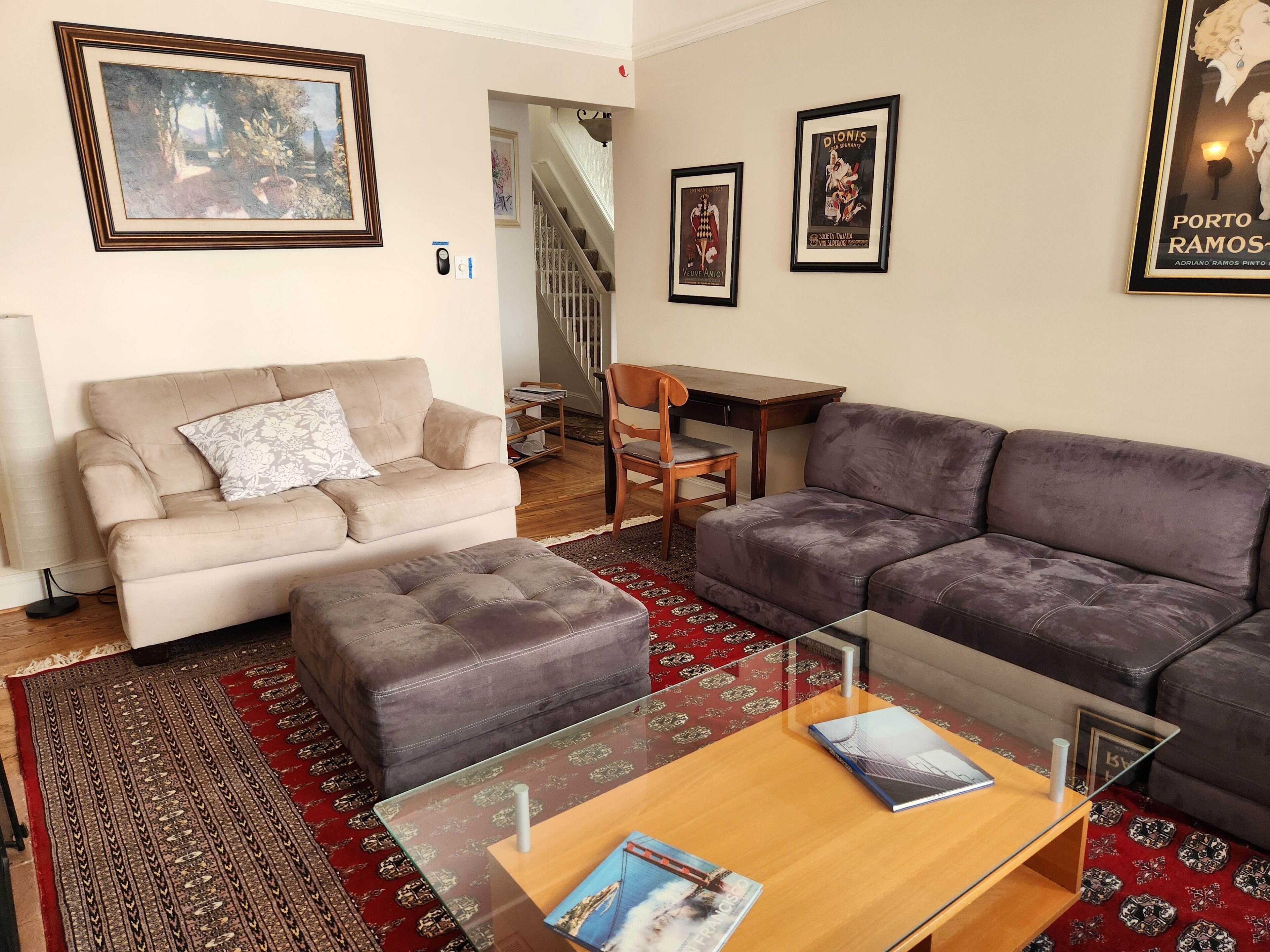 A living room with a beige sofa, a grey sofa, a glass coffee table, and a patterned rug.