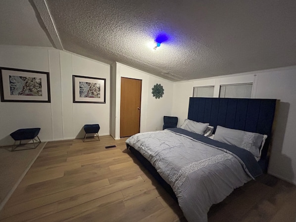 Une chambre à coucher avec un lit, une porte, deux chaises et des œuvres d’art encadrées accrochées aux murs.