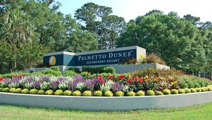 Señal de Palmetto Dunes Oceanfront Resort rodeada por un jardín ajardinado.