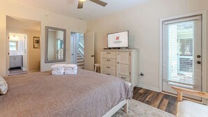 Un dormitorio con cama, ventilador de techo, televisor, cómoda y una puerta con persianas.