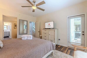 Ein Schlafzimmer mit einem Bett, einem Deckenventilator, einem Fernseher, einer Kommode und einer Tür mit Jalousien.