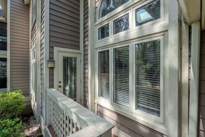 Ein Haus mit einer Veranda, einem weißen Geländer und einem Fenster mit Jalousien.
