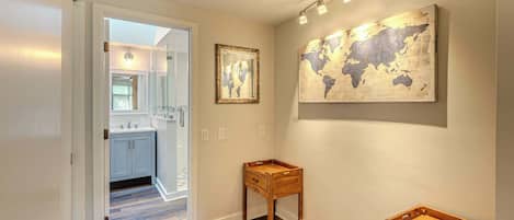Un couloir doté d’un plancher en bois, une petite table en bois, une œuvre d’art représentant une carte du monde et une cuisine visible à travers une porte ouverte.
