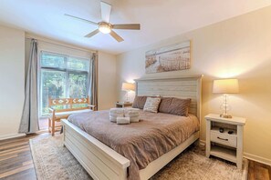 Ein Schlafzimmer mit einem Bett, einem Nachttisch, einer Lampe, einem Deckenventilator und einem Fenster mit Jalousien.