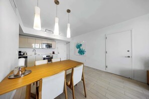 A modern kitchen with white cabinets, a wooden dining table, and pendant lights. - New! Beachwalk Resort 1BR Ocean & Beach access (Hallandale Beach)