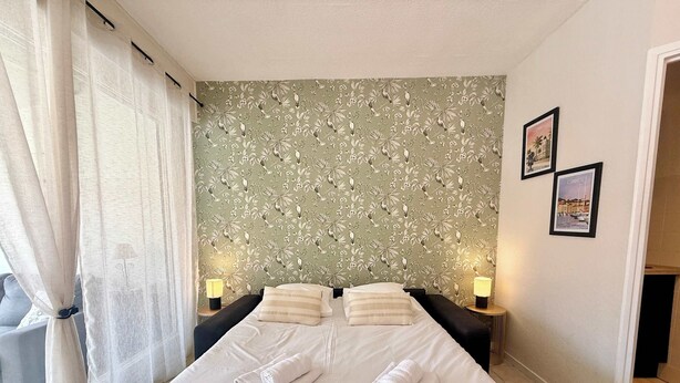 A hotel room with a large bed, two bedside tables with lamps, a floral wallpaper, and two framed pictures on the wall. - A052 Cosy studio near Croisette and the beach (Cannes)