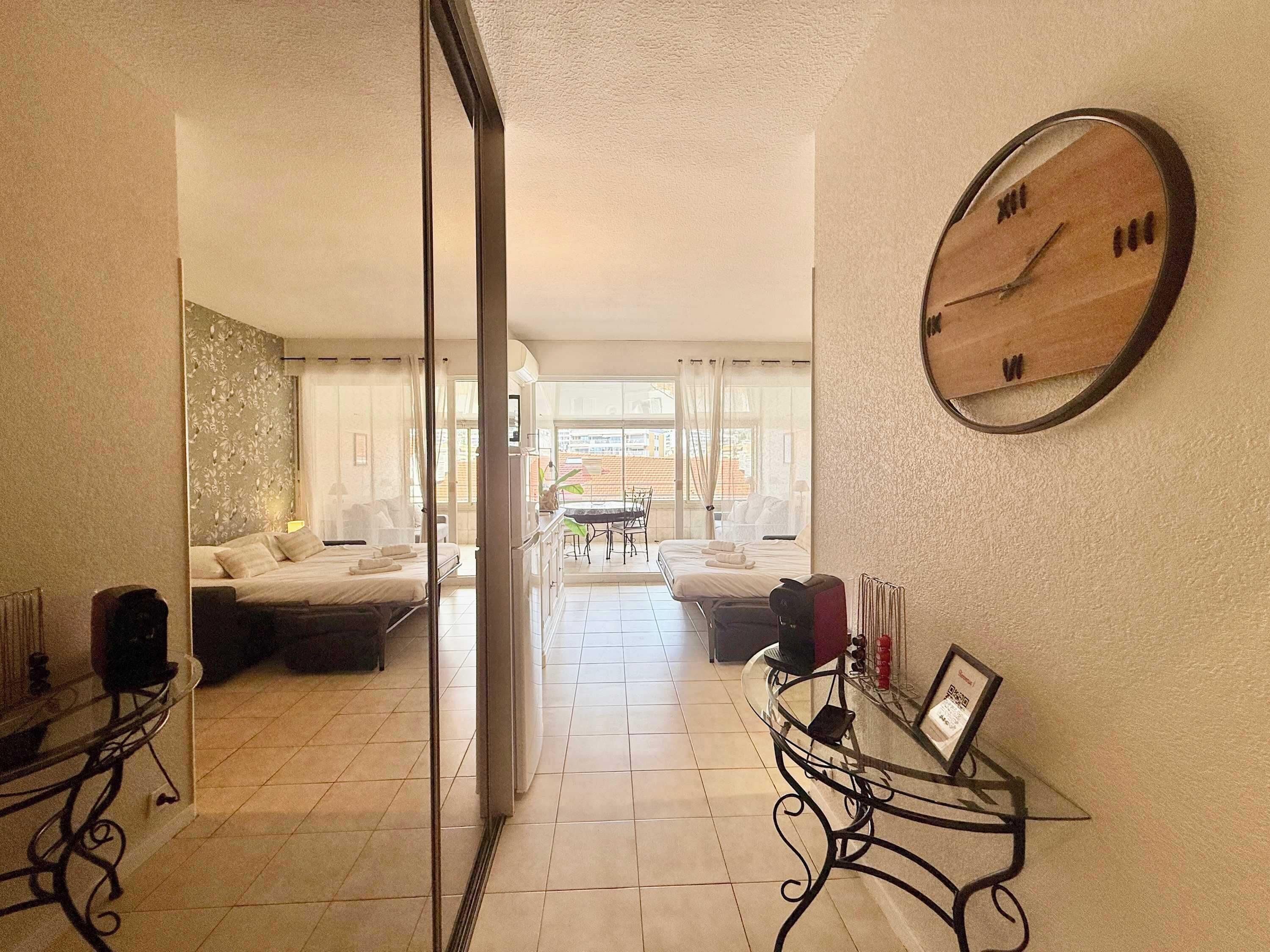 Une chambre d’hôtel comprenant un lit, un coin salon avec une table et des chaises, une grande horloge murale et une vue sur l’extérieur par une porte vitrée.