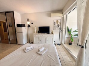 A hotel room with a bed, a television, a minibar, a desk, and a large window with curtains. - A052 Cosy studio near Croisette and the beach (Cannes)