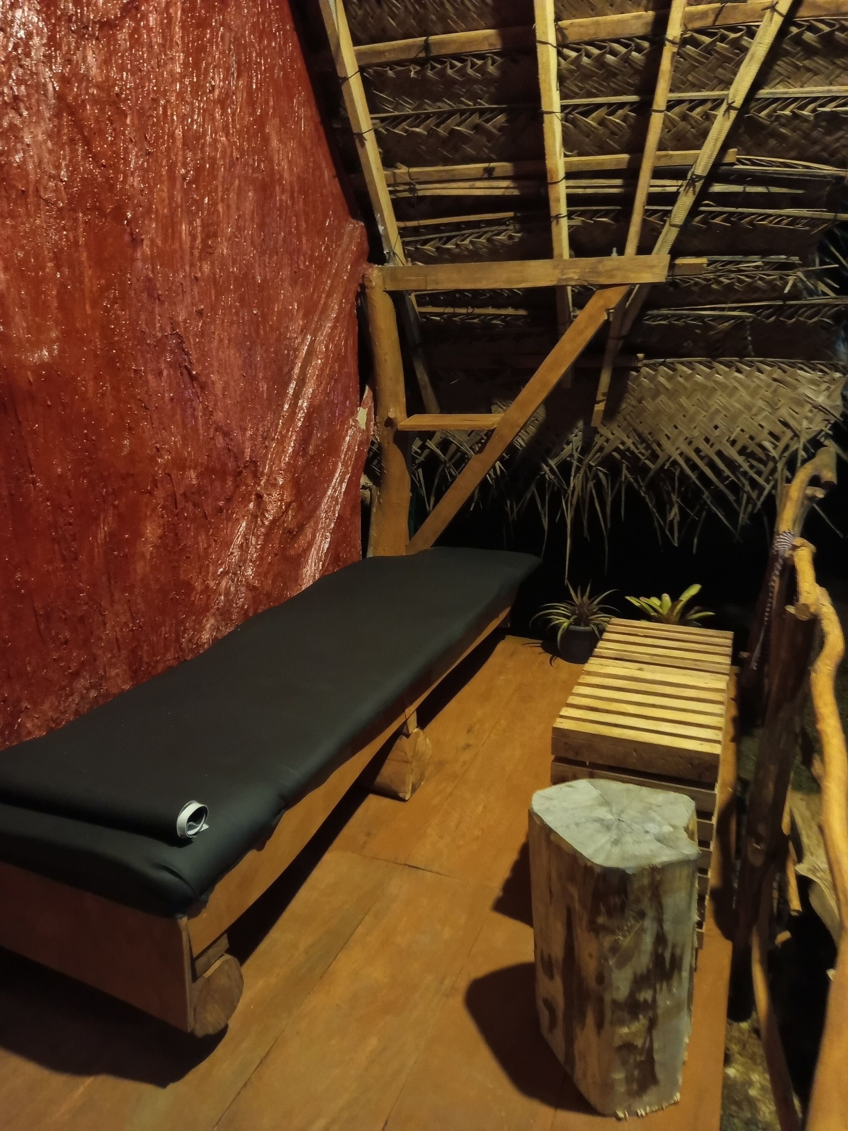 A room with a wooden bench, a small table, and a thatched roof structure.