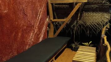 A room with a wooden bench, a small table, and a thatched roof structure.
