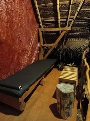 A room with a wooden bench, a small table, and a thatched roof structure.