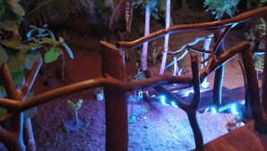 Una terraza de madera con barandilla, rodeada de plantas y árboles.
