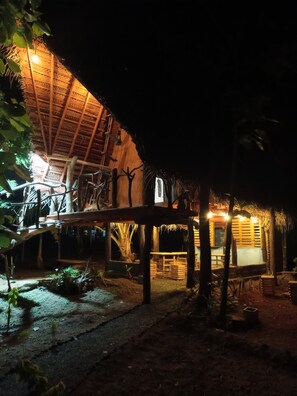 A thatched-roof structure with a wooden deck and a small white building, surrounded by trees and vegetation. - SIGIRI HUNTER'S ECO TREE LODGE AND Restu (Sigiriya,Dambulla)