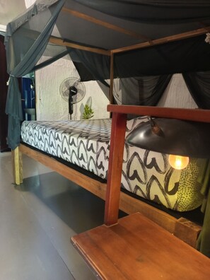 A single bed with a patterned bedspread, a bedside lamp, and a wall-mounted fan. - SIGIRI HUNTER'S ECO TREE LODGE AND Restu (Sigiriya,Dambulla)