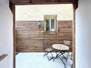 Eine Terrasse im Freien mit einem Holztisch und Stühlen, einem kleinen Fenster mit einer Pflanze und einem Holzzaun.