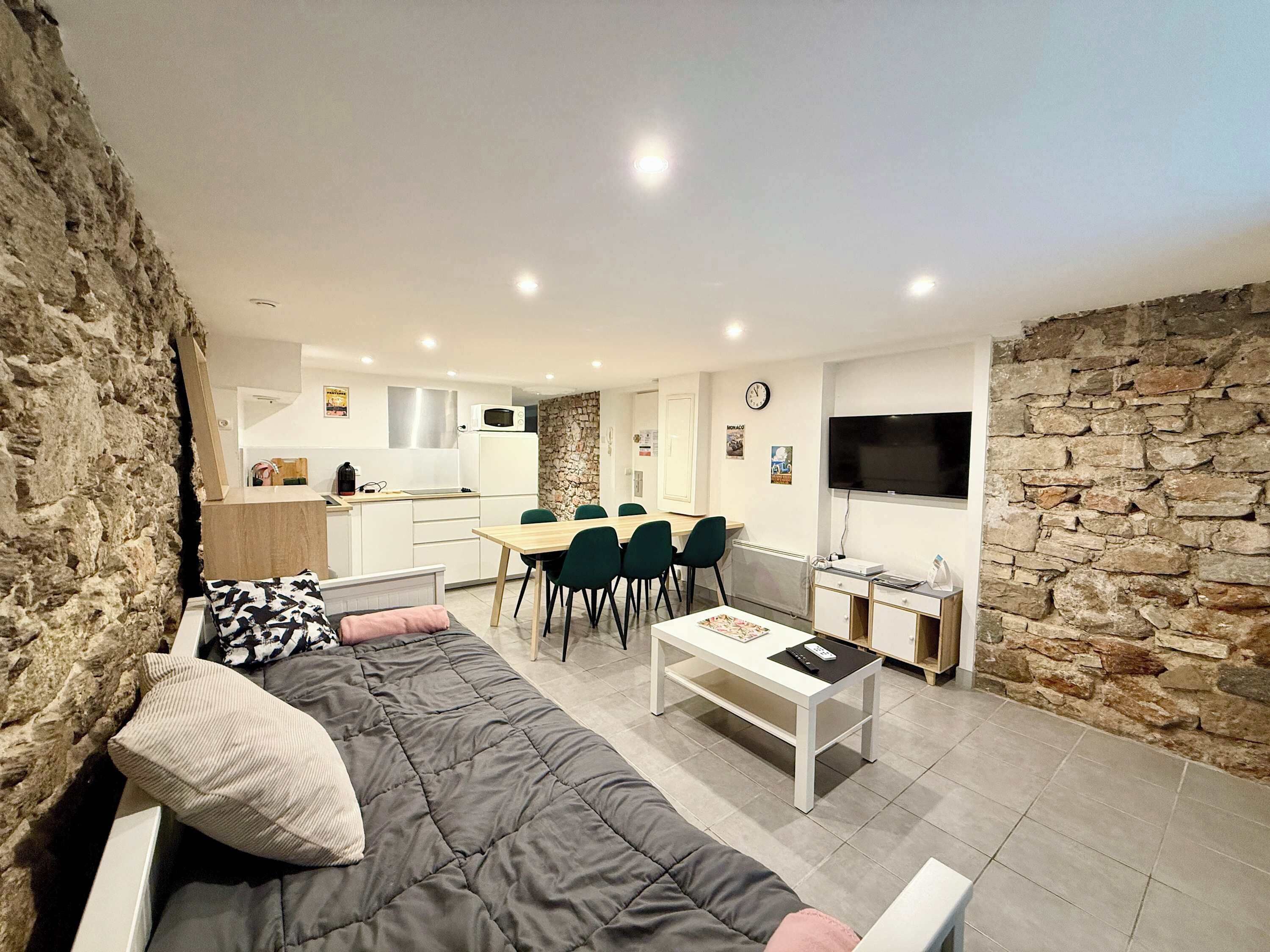 A modern living room with a sofa, a dining area with chairs, a kitchen with a microwave, and a stone wall.