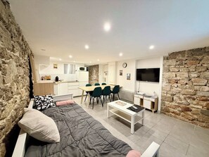 Ein modernes Wohnzimmer mit einer Couch, einem Essbereich mit Stühlen, einer Küche mit Mikrowelle und einer Steinwand.