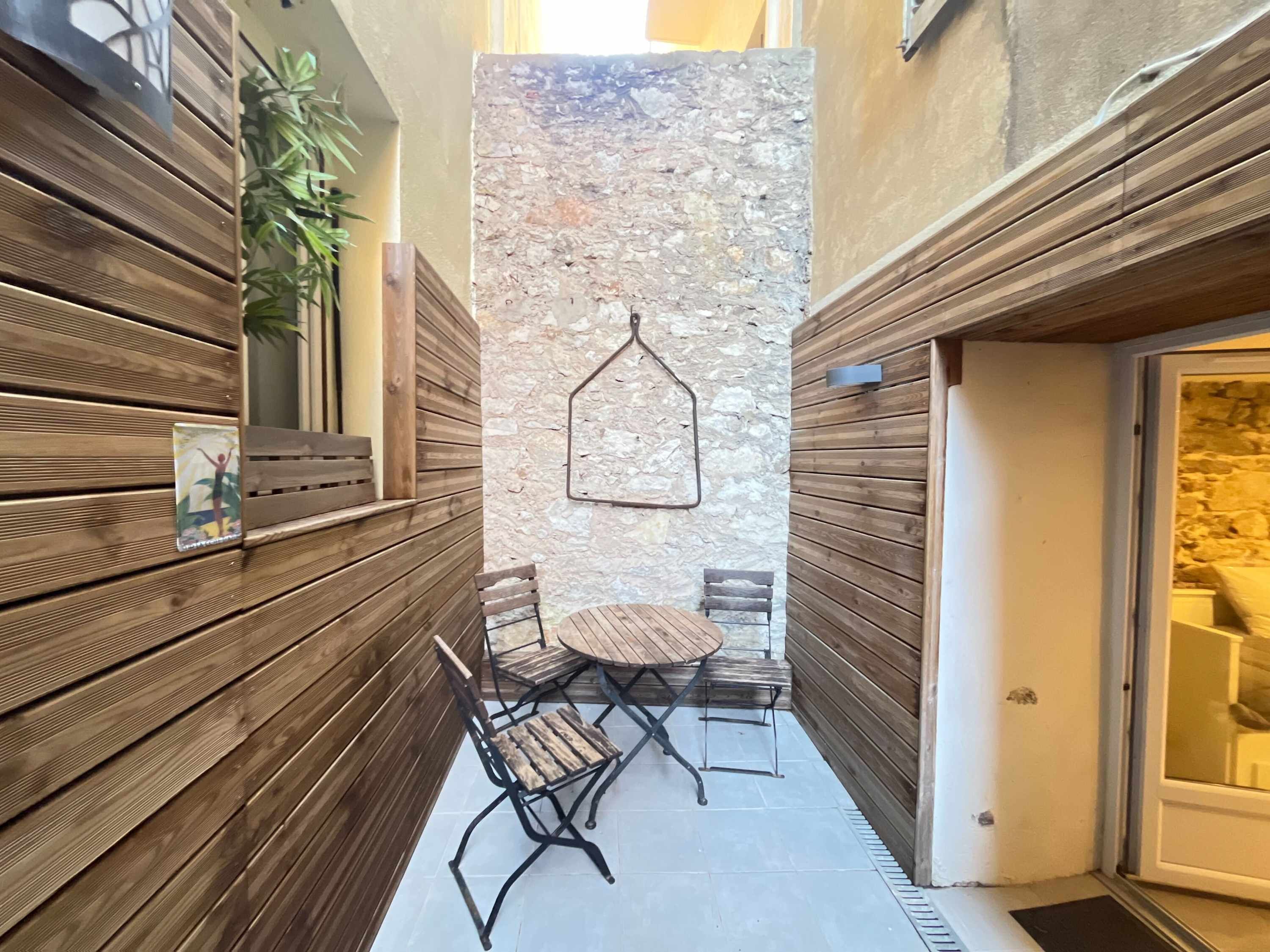 A narrow outdoor corridor with wooden paneling, a stone wall, and a small round table with chairs.
