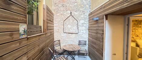 A narrow outdoor corridor with wooden paneling, a stone wall, and a small round table with chairs.