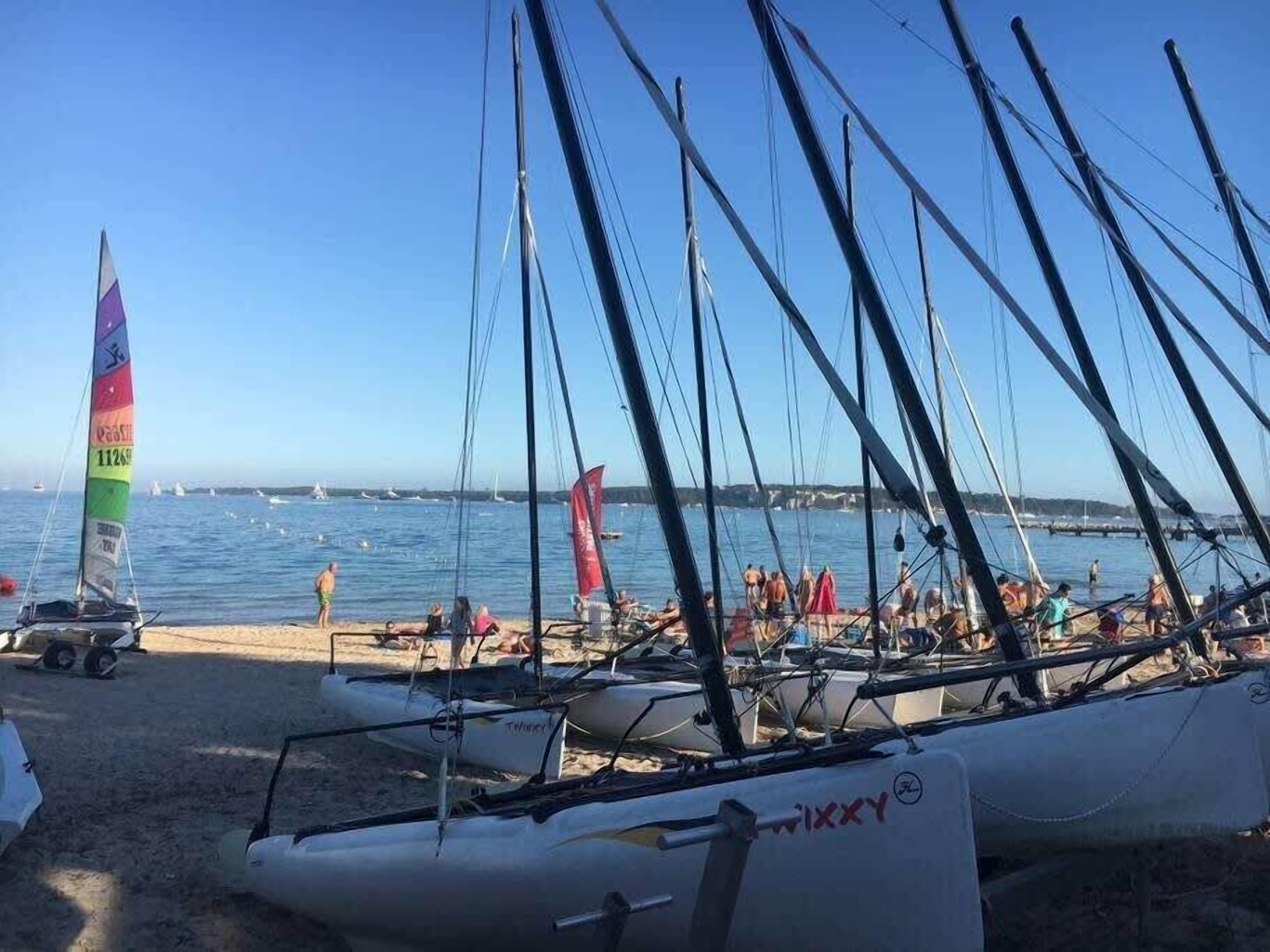 Ein Strand mit vor Anker liegenden Segelbooten und Menschen im Sand.